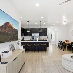 Open-concept living room and kitchen with a wall-mounted TV showing a canyon image, black kitchen island, and bar stools at the counter.