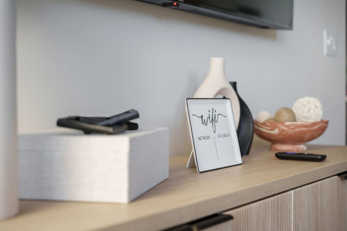 Framed white WiFi password card on a wooden console table, surrounded by vases, a decorative bowl, and remotes.