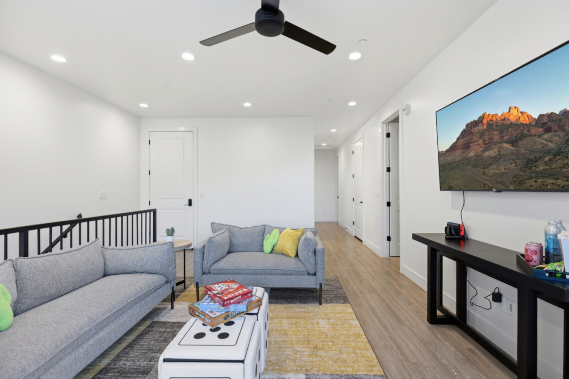 Bright modern living room with two gray sofas, colorful cushions, and a wall-mounted TV.