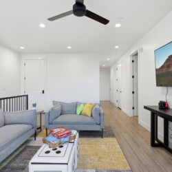 Bright modern living room with two gray sofas, colorful cushions, and a wall-mounted TV.