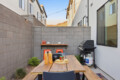 Backyard patio with a wooden dining table, grill, string lights, and gray brick walls in an urban courtyard.