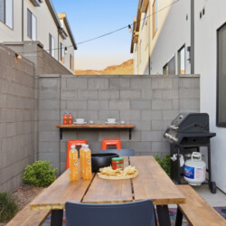 Backyard patio with a wooden dining table, grill, string lights, and gray brick walls in an urban courtyard.