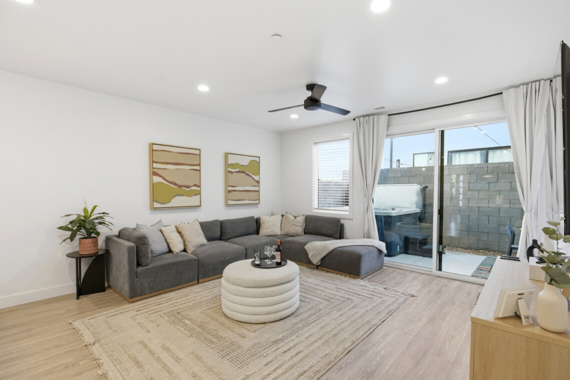 Cozy modern living room with a gray sectional sofa, beige pillows, and a round tufted coffee table on a woven rug.