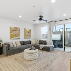 Cozy modern living room with a gray sectional sofa, beige pillows, and a round tufted coffee table on a woven rug.