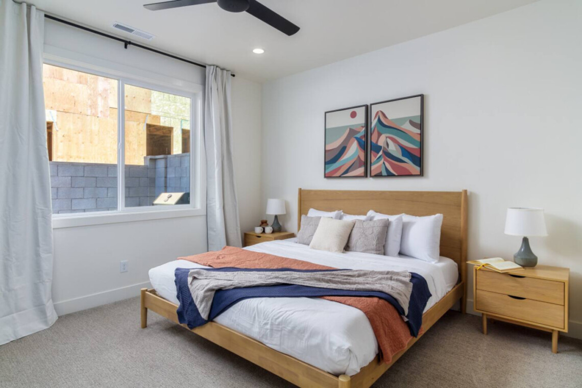 Modern bedroom with a wooden bed, two matching nightstands, lamps, and two-panel abstract mountain art above the headboard.