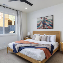 Modern bedroom with a wooden bed, two matching nightstands, lamps, and two-panel abstract mountain art above the headboard.