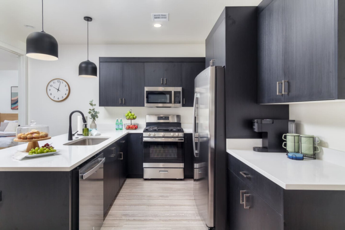 Modern kitchen with dark navy cabinets, white countertops, and a large island with stainless appliances.