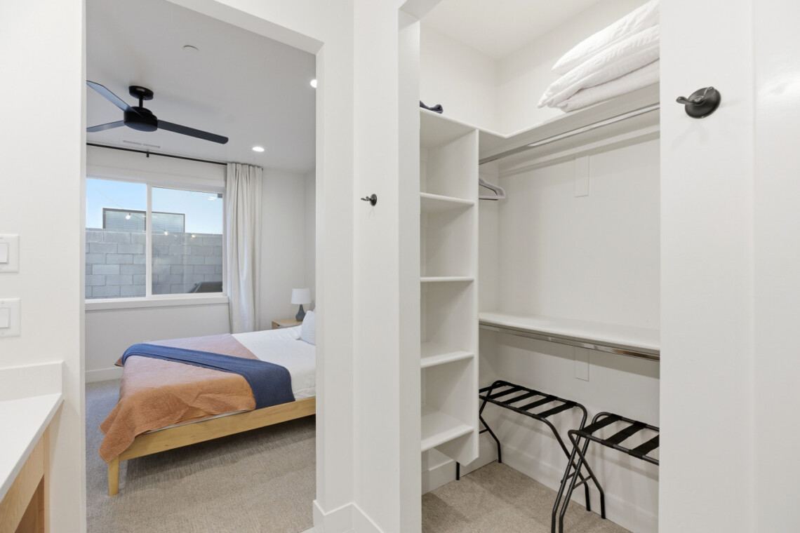 Bedroom with a wooden platform bed and peach-and-navy bedding, seen from an adjacent walk-in closet area.