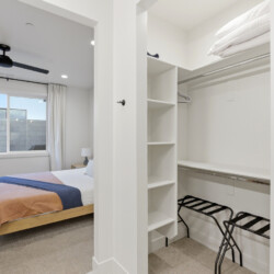 Bedroom with a wooden platform bed and peach-and-navy bedding, seen from an adjacent walk-in closet area.