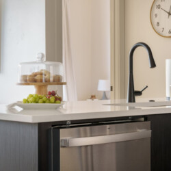 Contemporary kitchen island with a black gooseneck faucet, a glass cake stand with pastries, and a fruit platter on a white countertop.