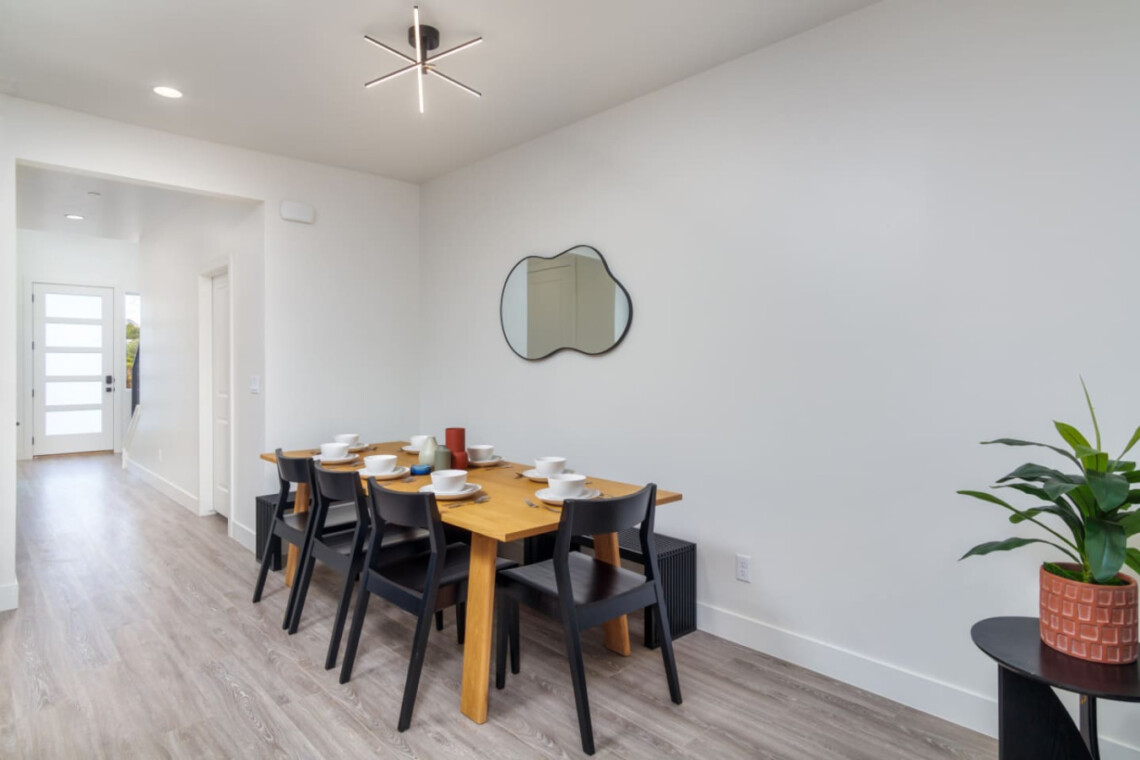 Modern dining room with a wooden six-seat table, black chairs, white dishes, and a cloud-shaped wall mirror.