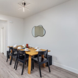 Modern dining room with a wooden six-seat table, black chairs, white dishes, and a cloud-shaped wall mirror.