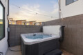 Outdoor hot tub in a concrete patio bordered by a tall gray block wall, string lights overhead at sunset/light dusk.
