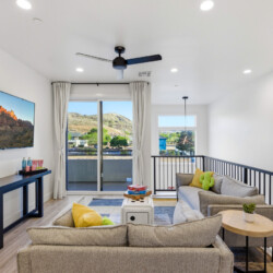 Living room with a wall-mounted TV, dark console, and beige sofas facing a sliding glass door to a balcony with hills outside.