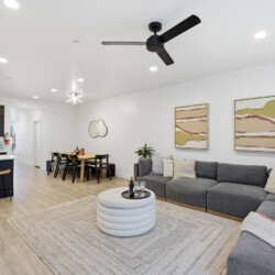 Open-plan living room and kitchen with a gray sectional sofa, abstract wall art, and a dining table in the background