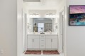 Bright, modern bathroom with a double sink vanity, large mirror, and matching white cabinets; two red bath mats on the floor and towels on the sides of the sinks.