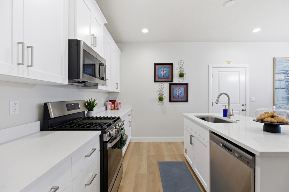 White modern kitchen with stainless steel stove, microwave, and dishwasher, and a large island with a sink and cake stand