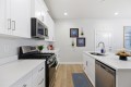 White modern kitchen with stainless steel stove, microwave, and dishwasher, and a large island with a sink and cake stand