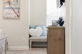 Cozy seating nook with a light beige loveseat, teal cushions, and a white heart pillow beside a wooden dresser by a window with blinds.
