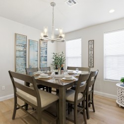 Dining room with a dark wood table for eight, beige upholstered chairs, and a chandelier overhead.