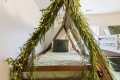 Wooden triangular bed frame under a canopy of hanging greenery with fairy lights and green bedding, creating a nature-inspired cozy bedroom atmosphere.
