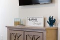 Decorative console with a framed quote reading 'kindness is always beautiful', a blue coral sculpture, and small boxed items on a light wood cabinet.