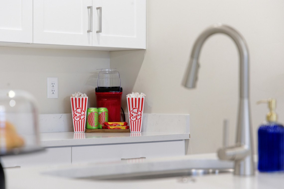 Kitchen counter with two red-and-white striped popcorn boxes flanking a red blender, plus green cans and a snack tray on the counter.