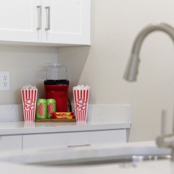Kitchen counter with two red-and-white striped popcorn boxes flanking a red blender, plus green cans and a snack tray on the counter.