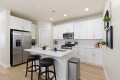 Bright white kitchen with a center island, stainless steel refrigerator, microwave, and bar stools at the island.