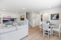 Bright open living room with a light gray sofa, white entertainment center, and a round dining table with chairs near a staircase.