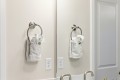 Two white towels with greenery hang from circular metal towel rings on a bathroom wall, mirrored by a split reflection of the sink area.