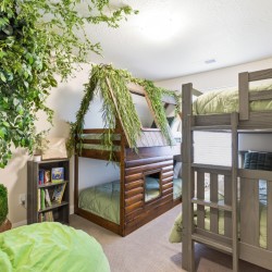 Kids' bedroom with gray bunk beds and a wooden treehouse-style play structure wrapped in greenery beside a small bookshelf.