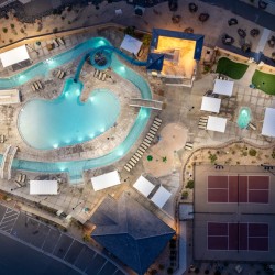 Aerial view of a resort pool area with a winding turquoise lazy river, multiple water slides, and surrounding lounge chairs and cabanas at dusk.