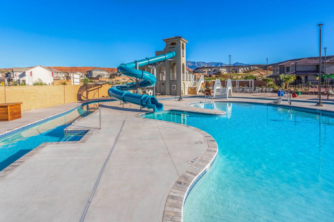 Outdoor community pool with a large blue twisting waterslide and lounge chairs under a bright blue sky.