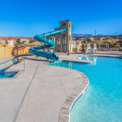 Outdoor community pool with a large blue twisting waterslide and lounge chairs under a bright blue sky.