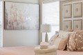 Blush pink bedroom with quilted bedspread, decorative pillows, stacked towels and a hat on the bed; beige tufted headboard and a framed tree artwork on the wall.