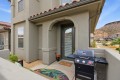 Front porch of a beige stucco townhouse with an arched entryway, glass door with blinds, and a black gas grill on the patio adjacent to the door.