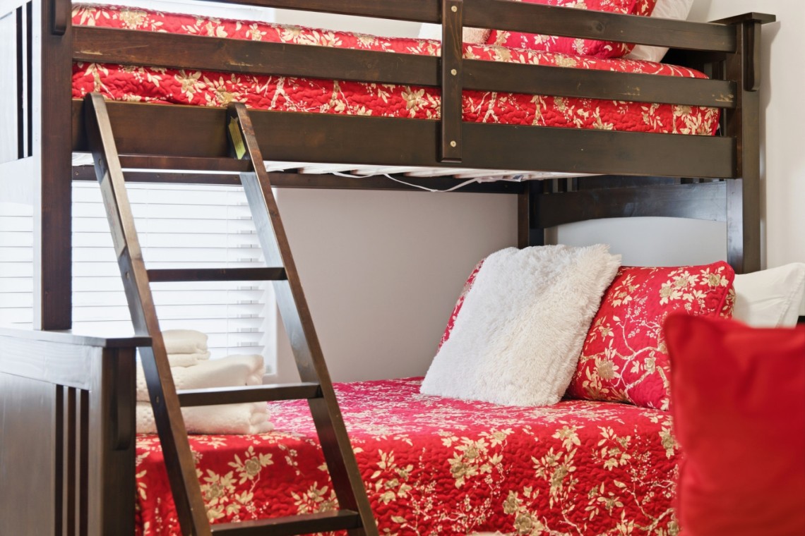 Dark wooden bunk bed with a red floral quilt, white fluffy pillow, and folded towels on the lower bunk.