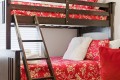 Dark wooden bunk bed with a red floral quilt, white fluffy pillow, and folded towels on the lower bunk.