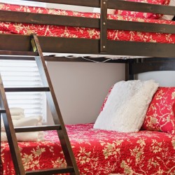 Dark wooden bunk bed with a red floral quilt, white fluffy pillow, and folded towels on the lower bunk.