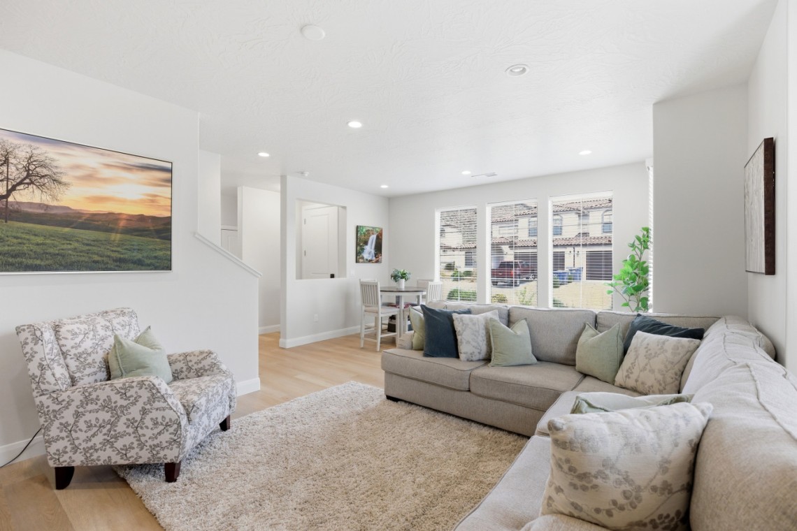 Bright open living room with a beige sectional, fluffy rug, and large windows filling the space with daylight.