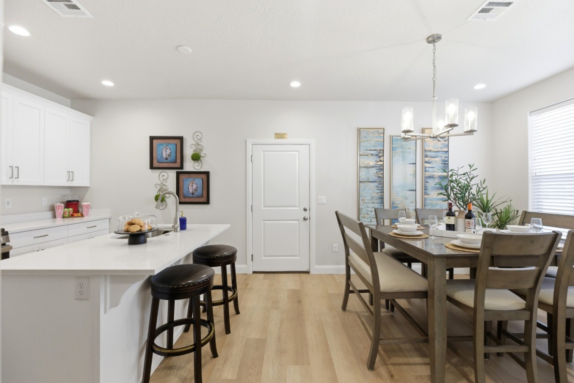 Open-concept kitchen and dining area with white cabinets, a long white island with two dark-stool seats, and a wooden table set for six under a chandelier.