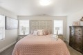 Bedroom with blush pink quilt, tufted headboard, two nightstands, and a tall ornate dresser across from the bed with lamps on each side