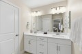 Double bathroom vanity with white cabinets, two sinks, and a large wall mirror with modern light fixtures above.