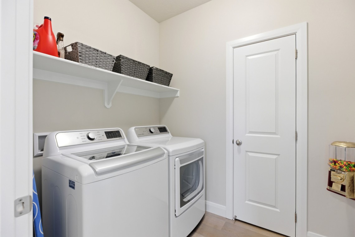 Laundry room with a white washer and dryer under a shelf holding wicker baskets