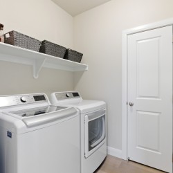 Laundry room with a white washer and dryer under a shelf holding wicker baskets