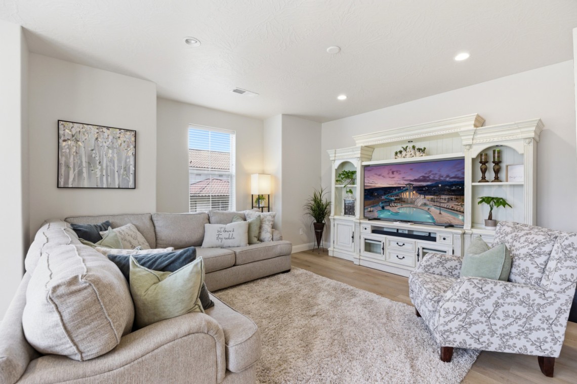 Bright living room with a beige sectional, patterned armchair, and a white ornate entertainment center housing a large TV.
