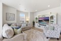 Bright living room with a beige sectional, patterned armchair, and a white ornate entertainment center housing a large TV.