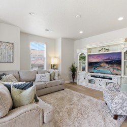 Bright living room with a beige sectional, patterned armchair, and a white ornate entertainment center housing a large TV.