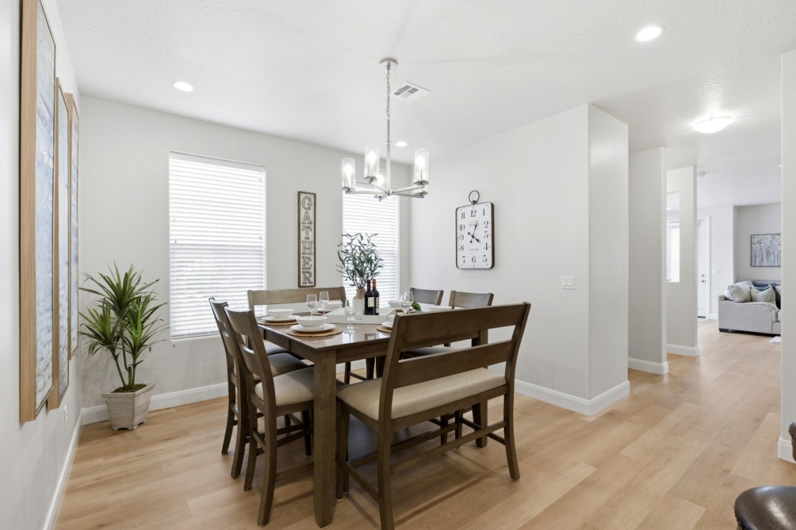 Dining room with a dark wood table set for six, a chandelier overhead, and a plant near the window.